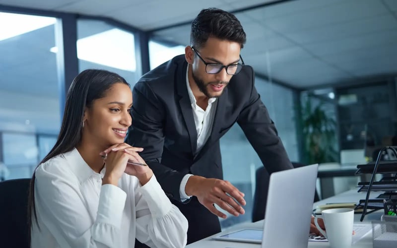 Two professionals collaborate on a laptop in an office, creating career development strategies for their organization.