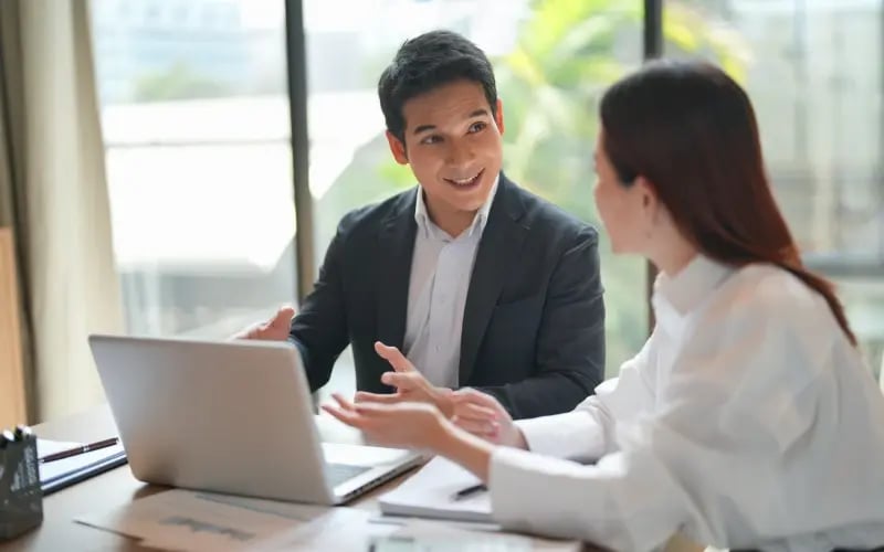 Manager and employee discuss career planning together at a desk with an open laptop in an office setting.