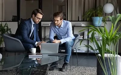 Corporate leadership coaching in a modern office setting: two men sit around a coffee table looking at a laptop.