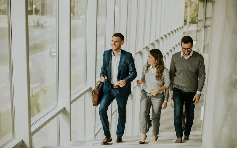 Three business professionals going through a career transition climb stairs in an office corridor 