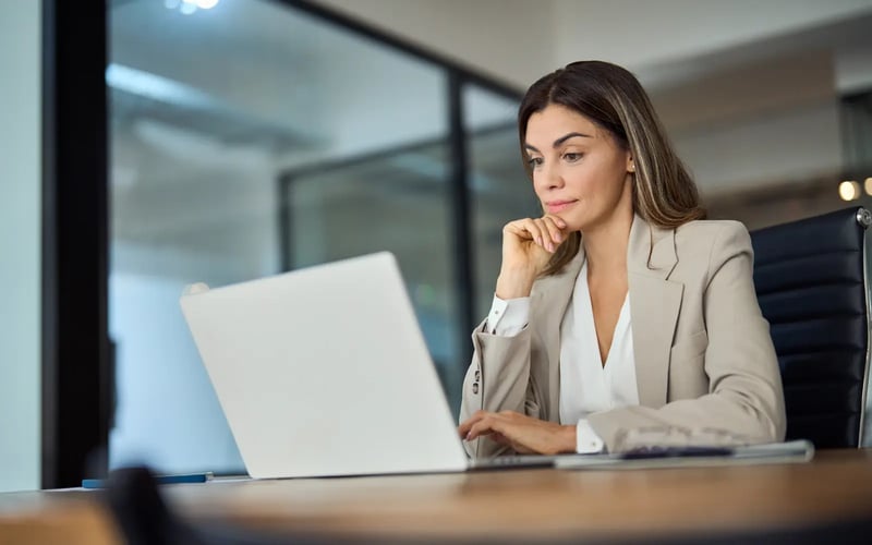 HR leader considers outplacement for tech layoffs while sitting at a desk and working on a laptop. 