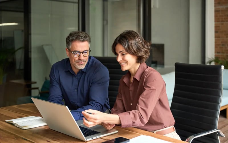 Two HR professionals collaborate at a desk on risk management and outplacement strategy using a laptop.