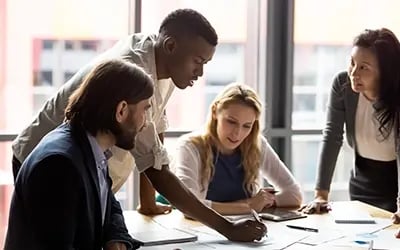 Employees collaborate around a table, reflecting a talent strategy focused on engagement and career development.