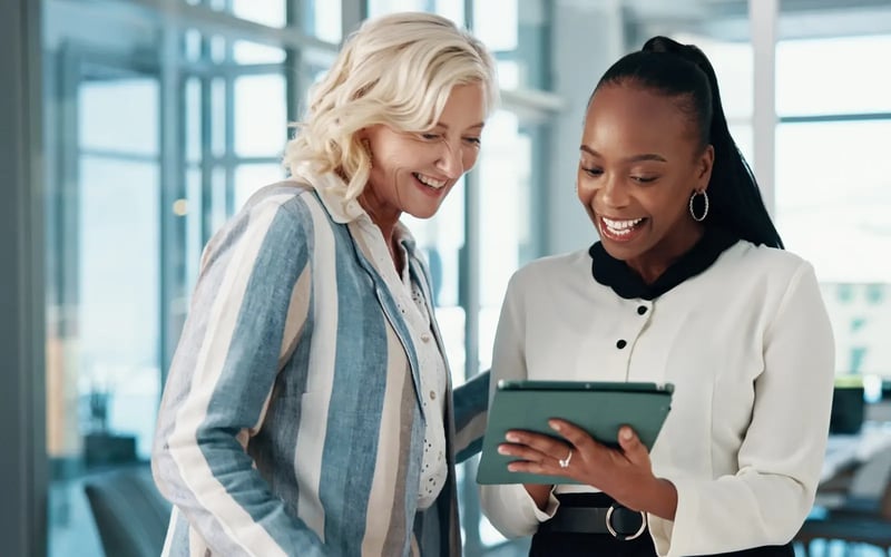 Smiling coworkers collaborate on a tablet, reflecting the success of workplace talent engagement strategies. 