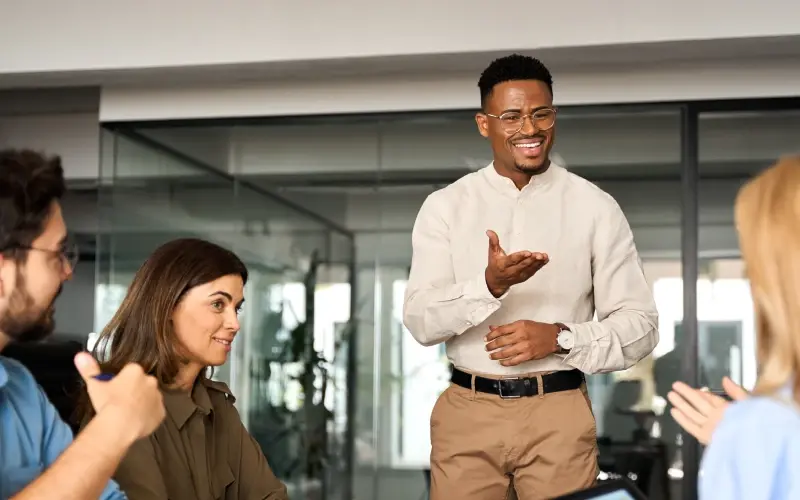 Man demonstrating digital leadership while leading a meeting with three seated employees around a conference table. 