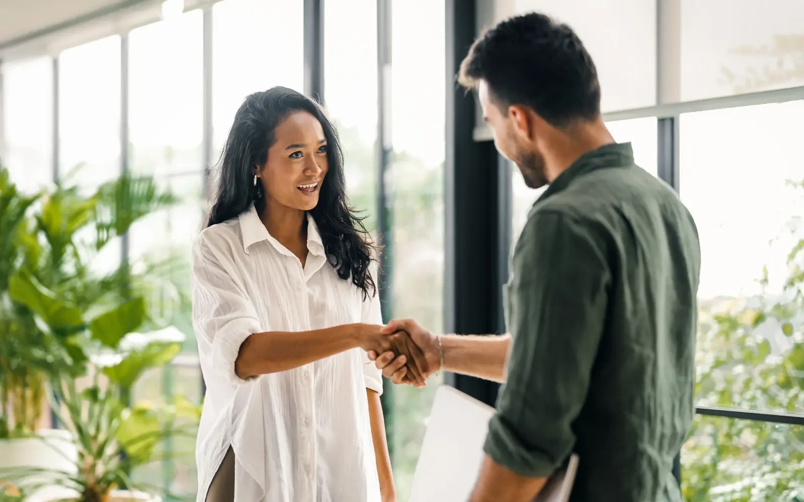 Executive coach greets coachee with a handshake before starting a session in a modern office setting. 