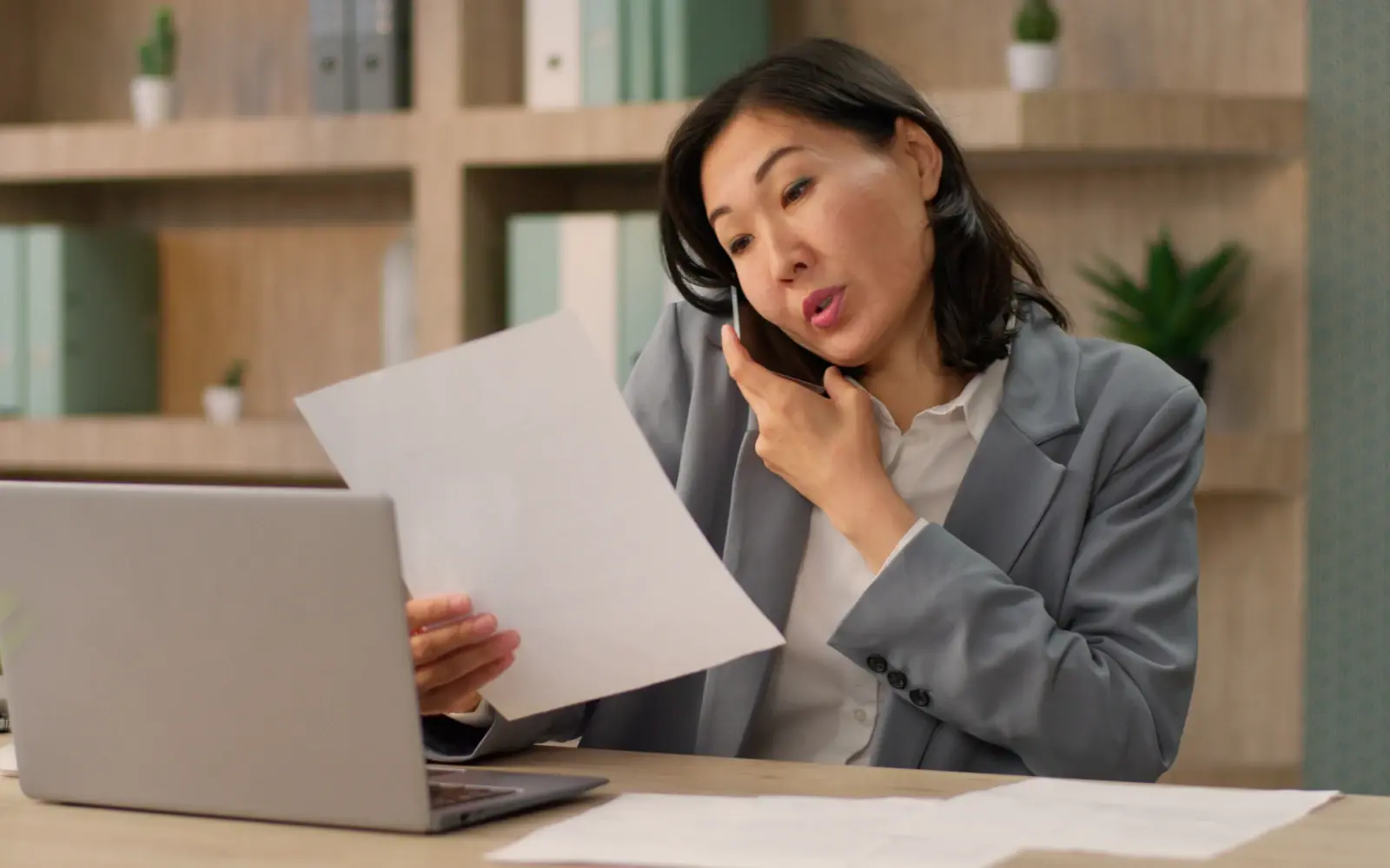CHRO at her desk evaluates talent solutions, reviewing documents and laptop during a phone call. 