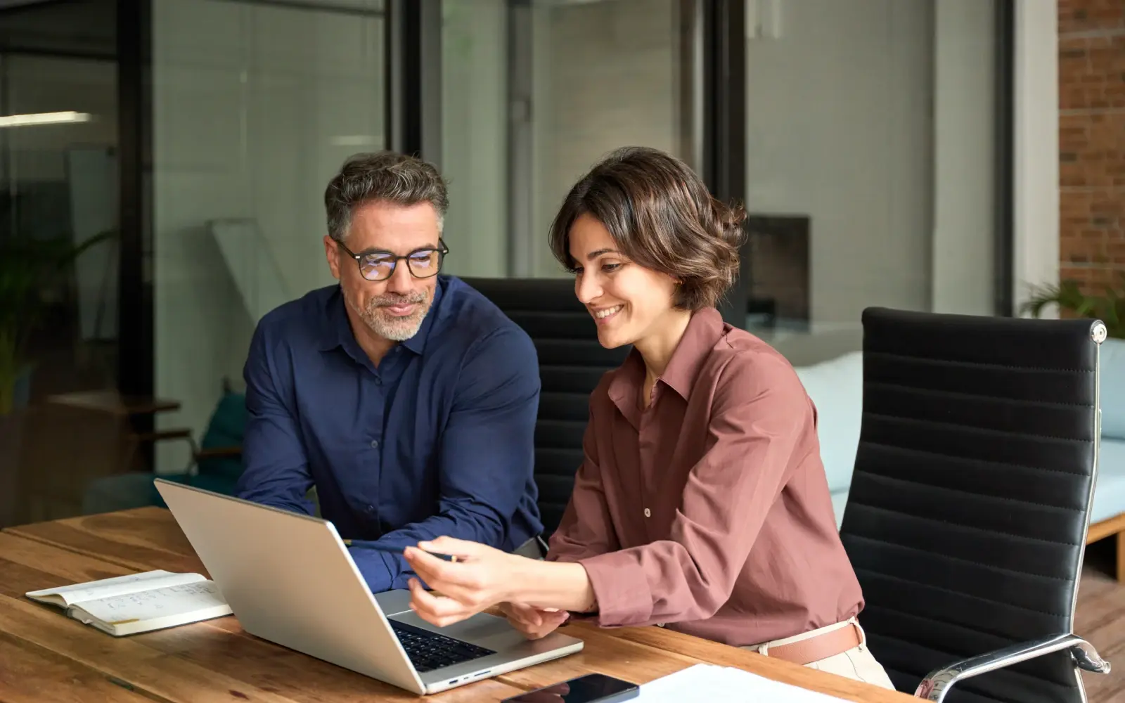 Two HR professionals collaborate at a desk on risk management and outplacement strategy using a laptop.